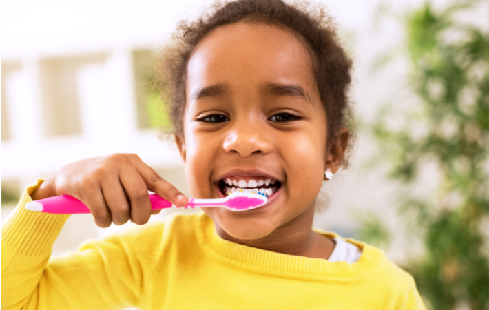 young girl smiling as she brushes her teeth