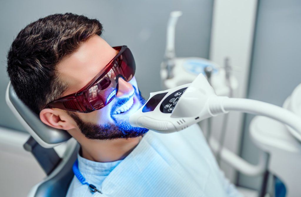 Smiling man having teeth whitened with light in dental office