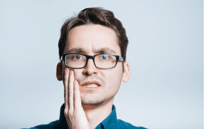 Man looking extremely worried holding his face due to a dental emergency