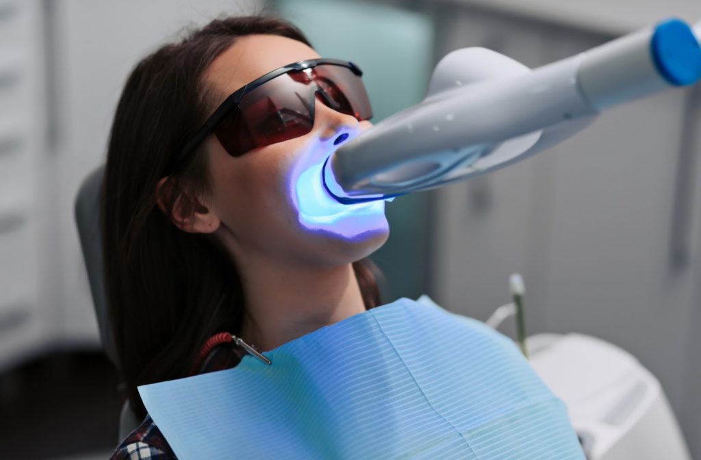 Woman in a dental chair getting her teeth whitened by an ultraviolet light