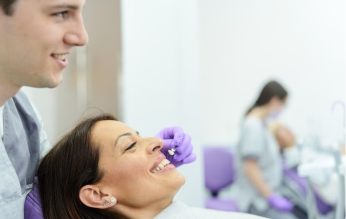 A dentist holding up a veneer to a patient while they choose the colour of her new veneers