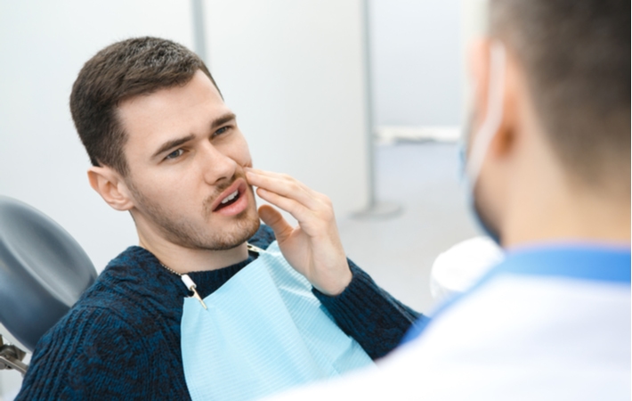 A man at the dentist discussing possible treatments for his infected tooth as he holds the left side of his face in pain