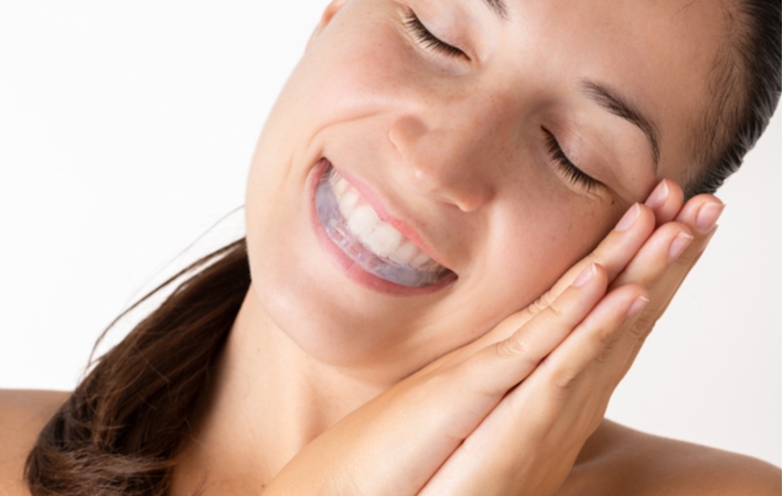 A woman making a sleeping gesture and wearing a bite plate in her mouth to help protect her teeth from grinding caused by bruxism