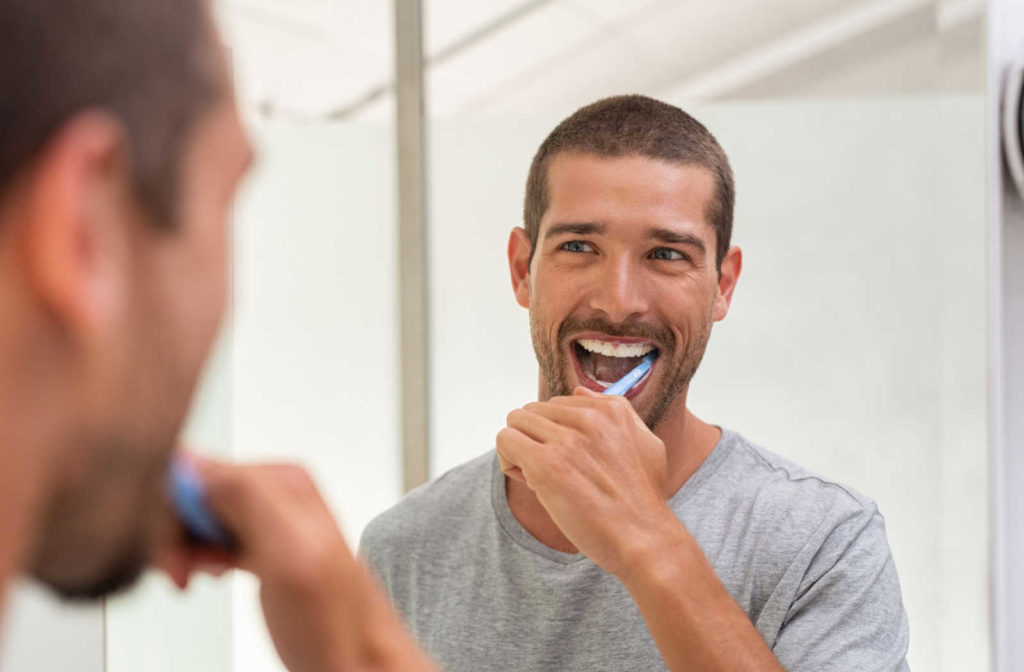 A male looking in a mirror brushing his teeth to help maintain good oral hygiene.