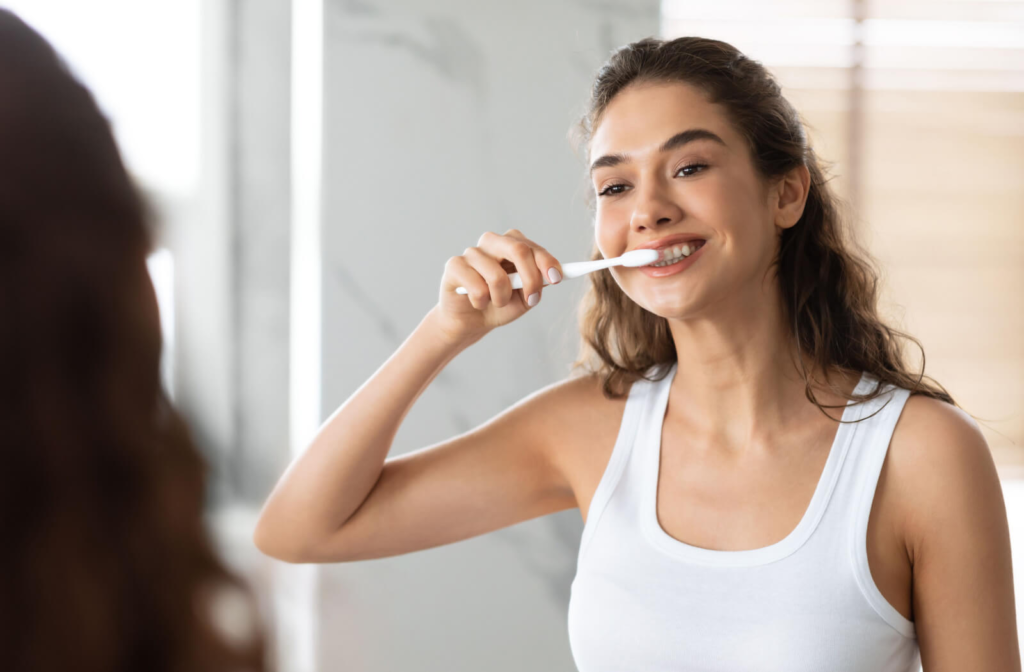 A young woman standing in front of a mirror brushing her teeth with a toothbrush.