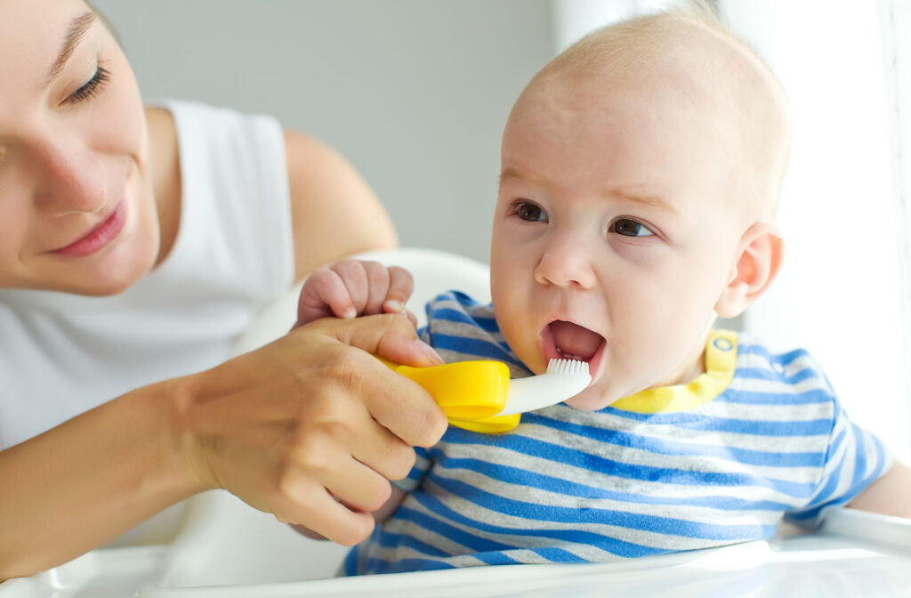 A woman using a soft-bristled toothbrush to brush the teeth of a baby.