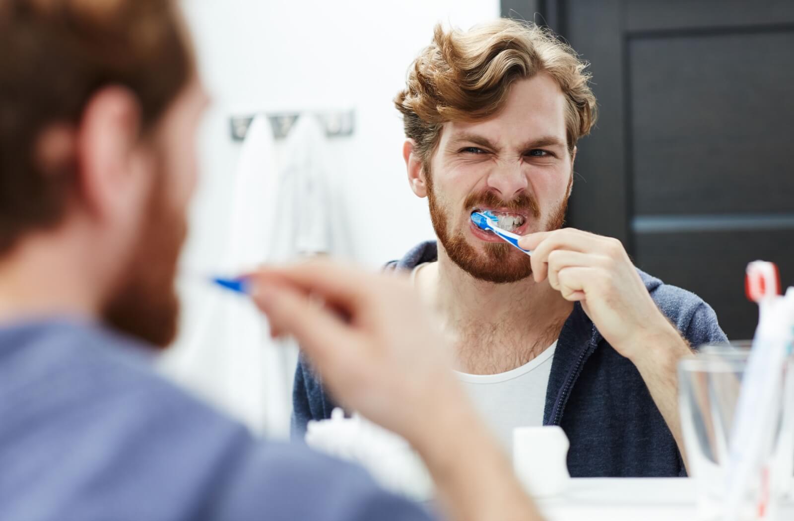A man brushing his teeth using a blue toothbrush in front of a mirror.
