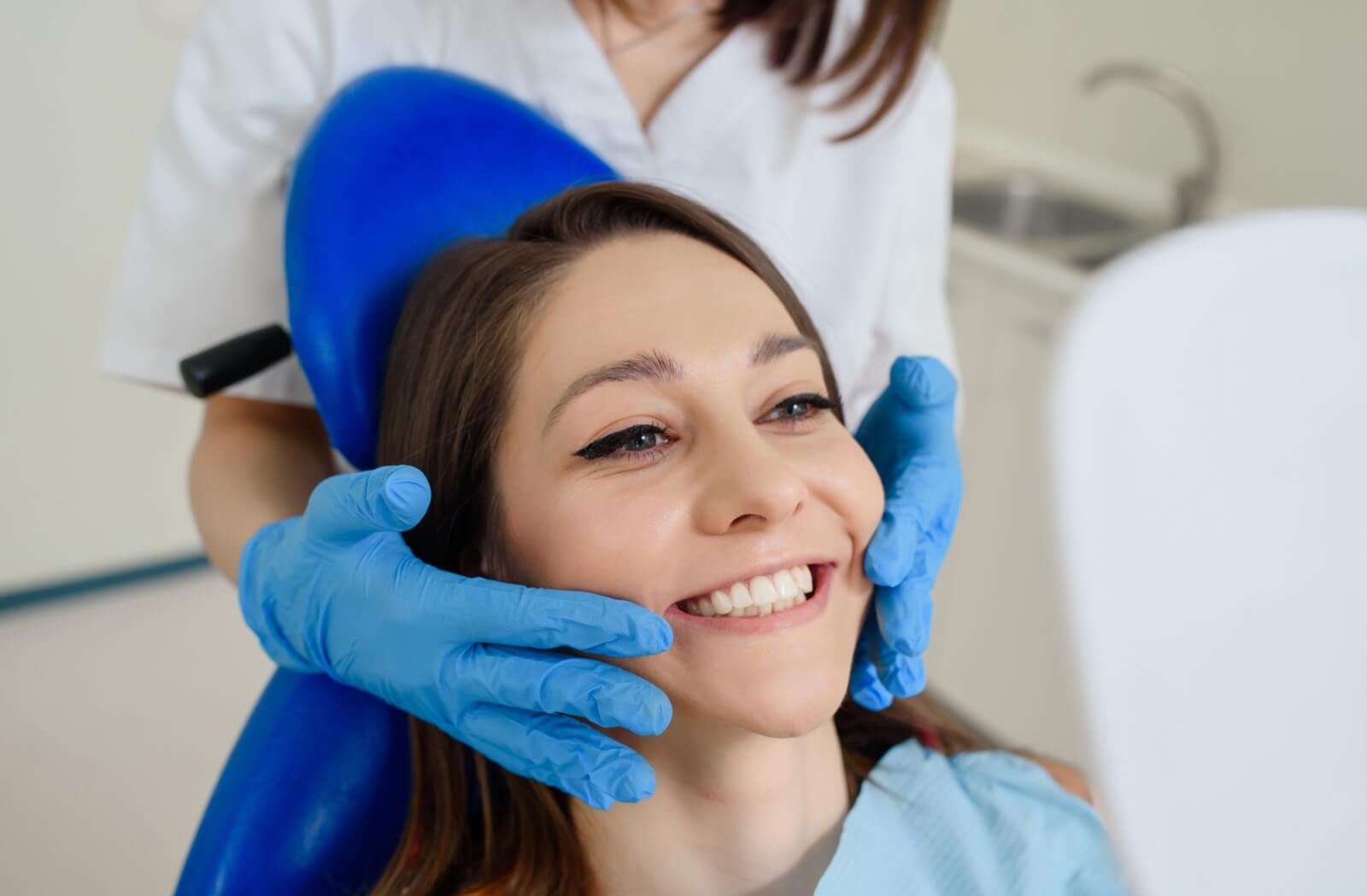 Young patient sitting on a dental chair looking into a mirror with a smile to check teeth as a dentist helps