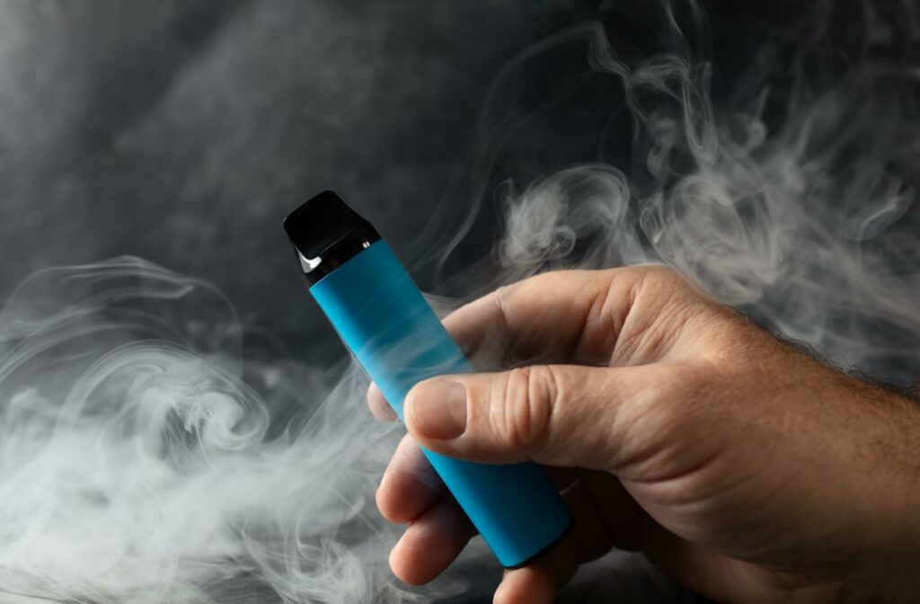 A person holds a vaping device in front of an ominous swirl of smoke.