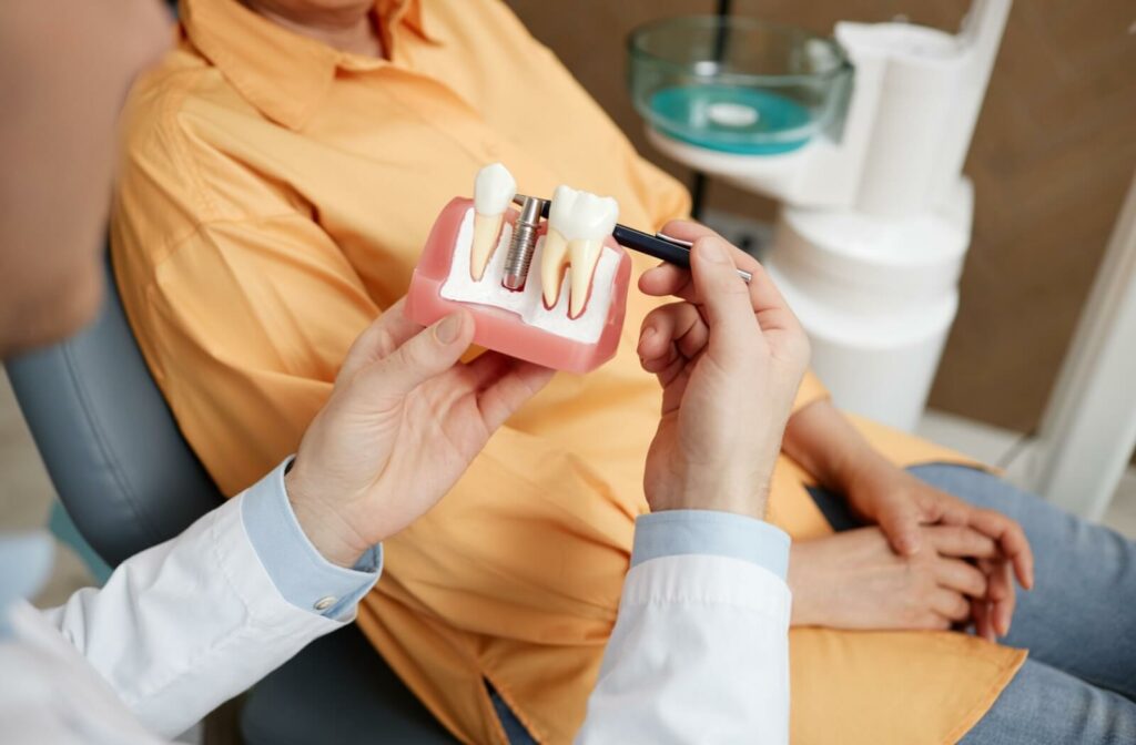 A patient sitting in an exam chair being shown a model of a dental implant.