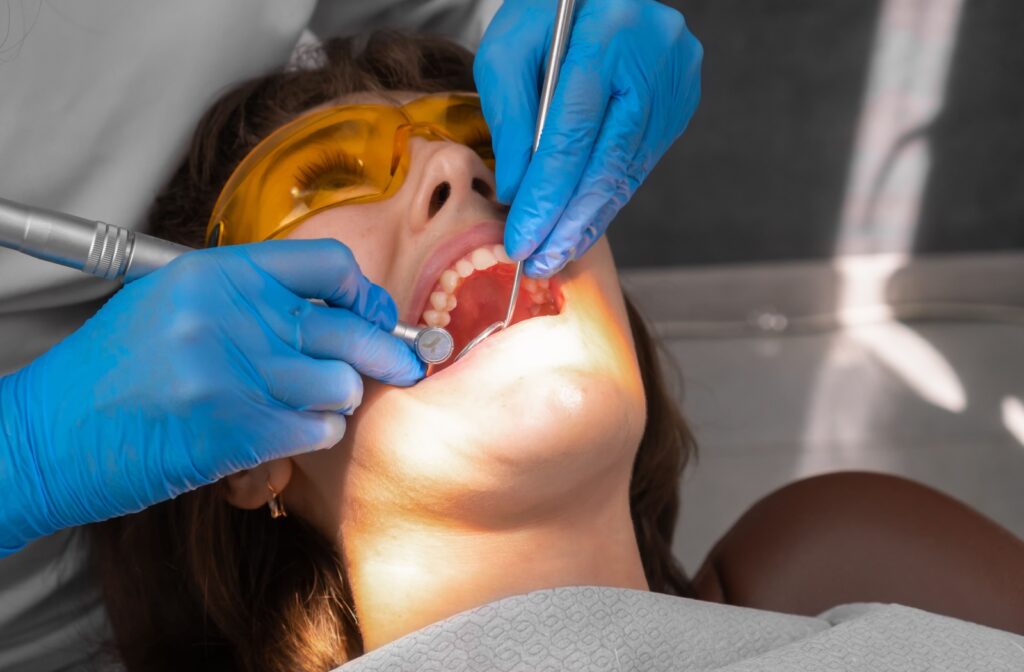 A patient laying down in a dental chair getting built up plaque scraped off their teeth.